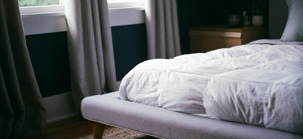 Letto con materasso e biancheria bianca vicino alla finestra